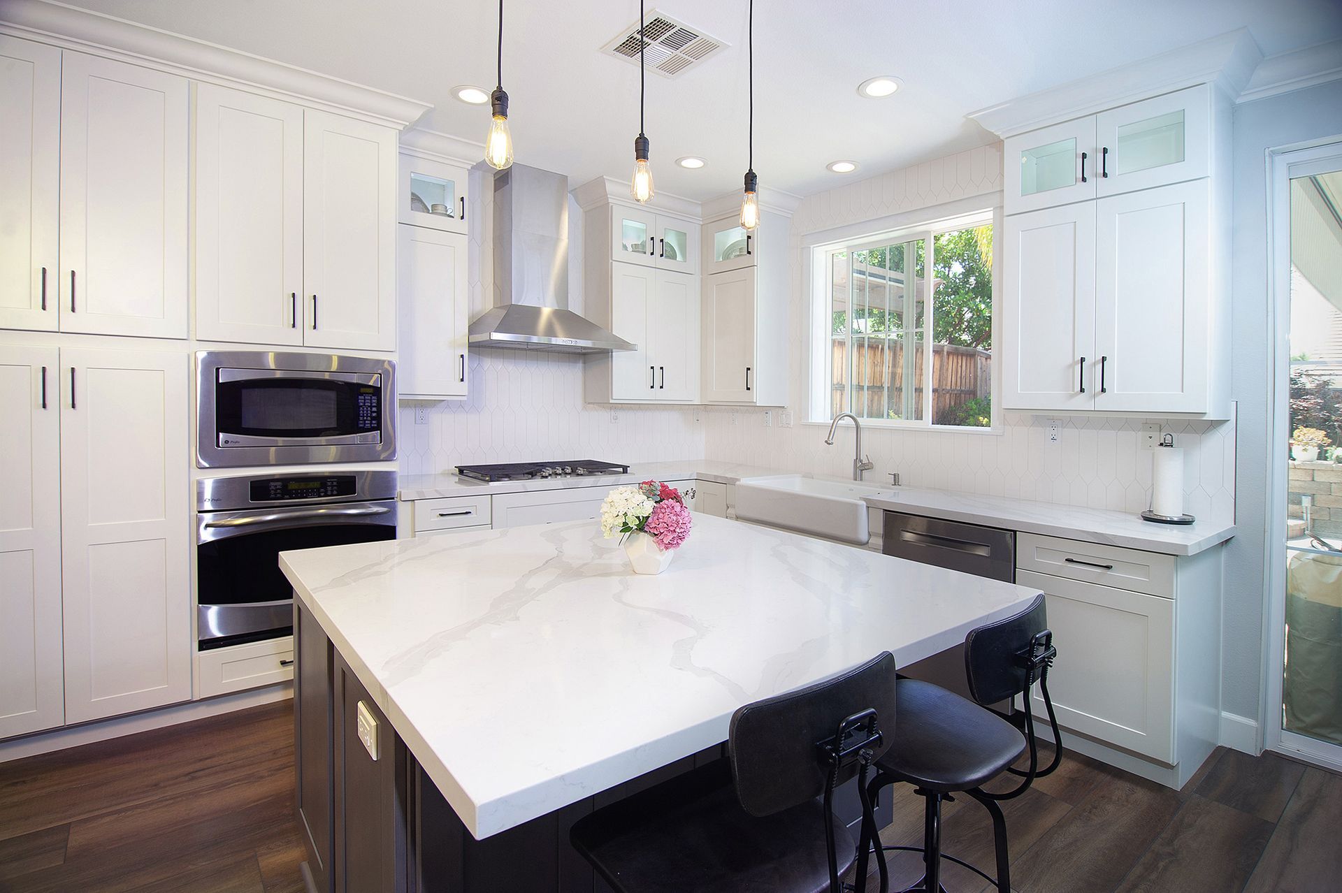 Modern white kitchen with island, stainless steel appliances, and pendant lights.