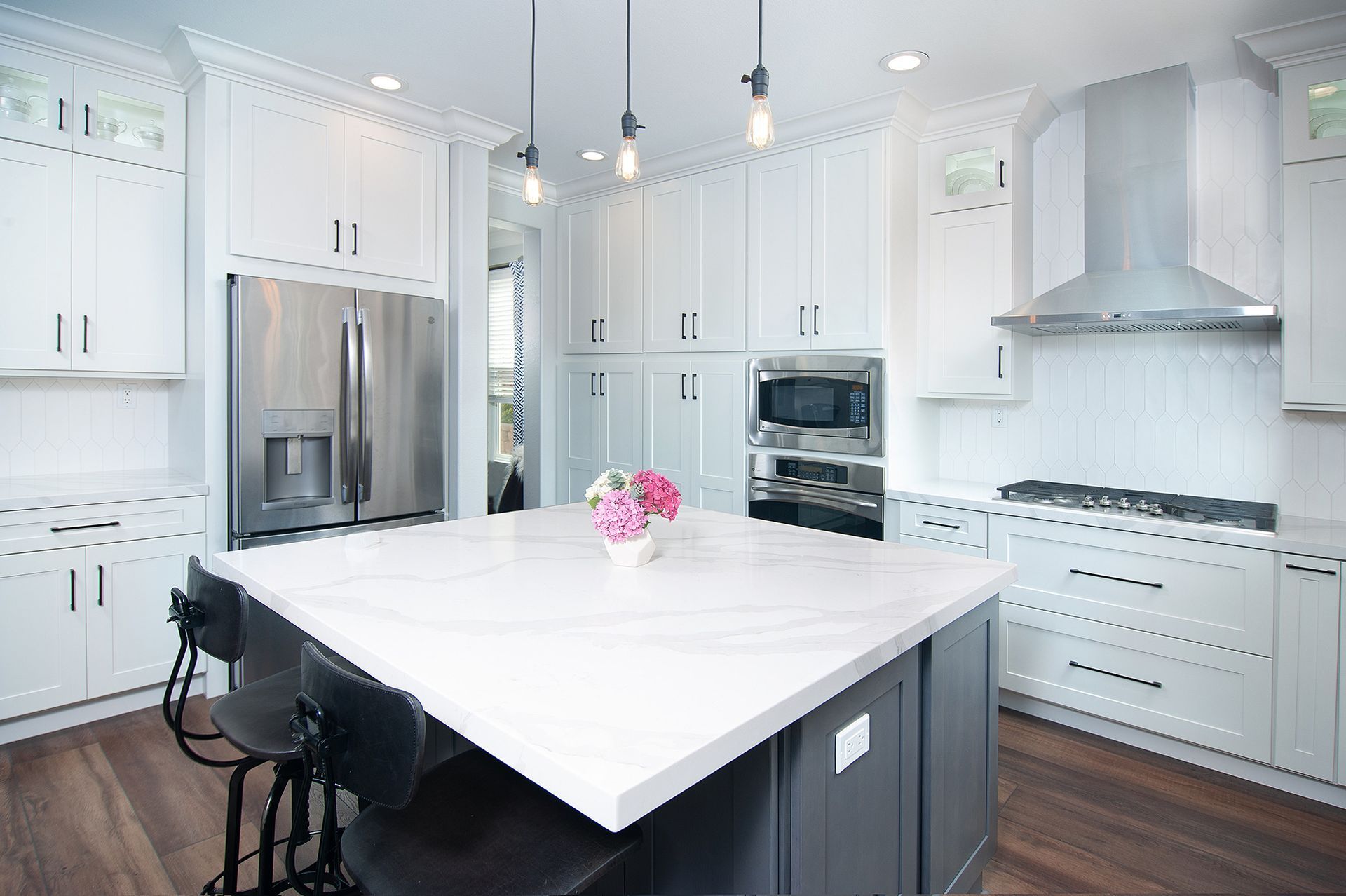 Modern white kitchen with an island, stainless steel appliances, and dark accents.