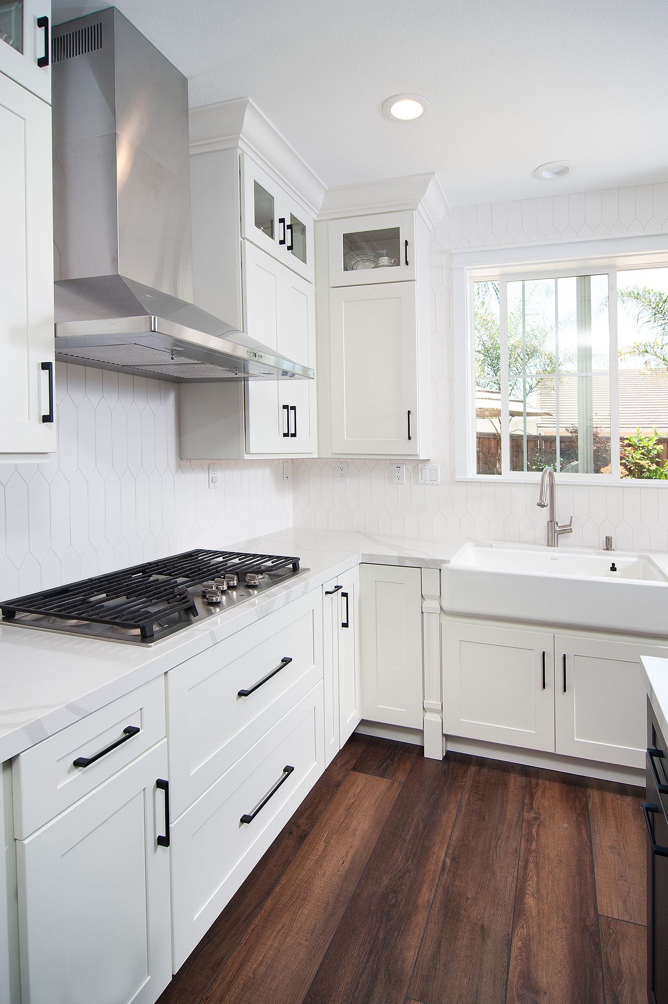White kitchen with stainless steel hood, gas stove, and farmhouse sink. Dark wood floor.