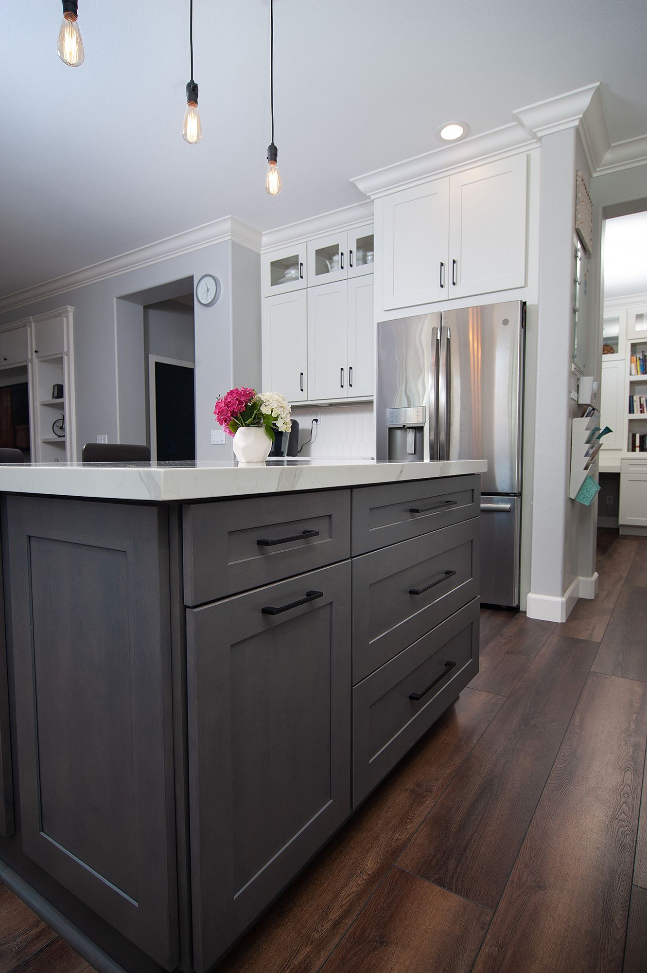 Gray kitchen island with dark cabinets, stainless steel refrigerator, and white upper cabinets.
