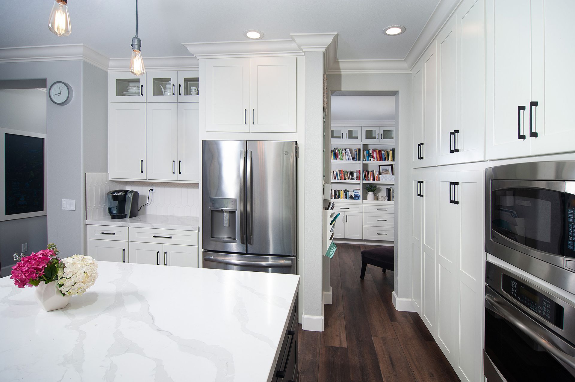 Modern white kitchen with stainless steel appliances and dark wood floors.