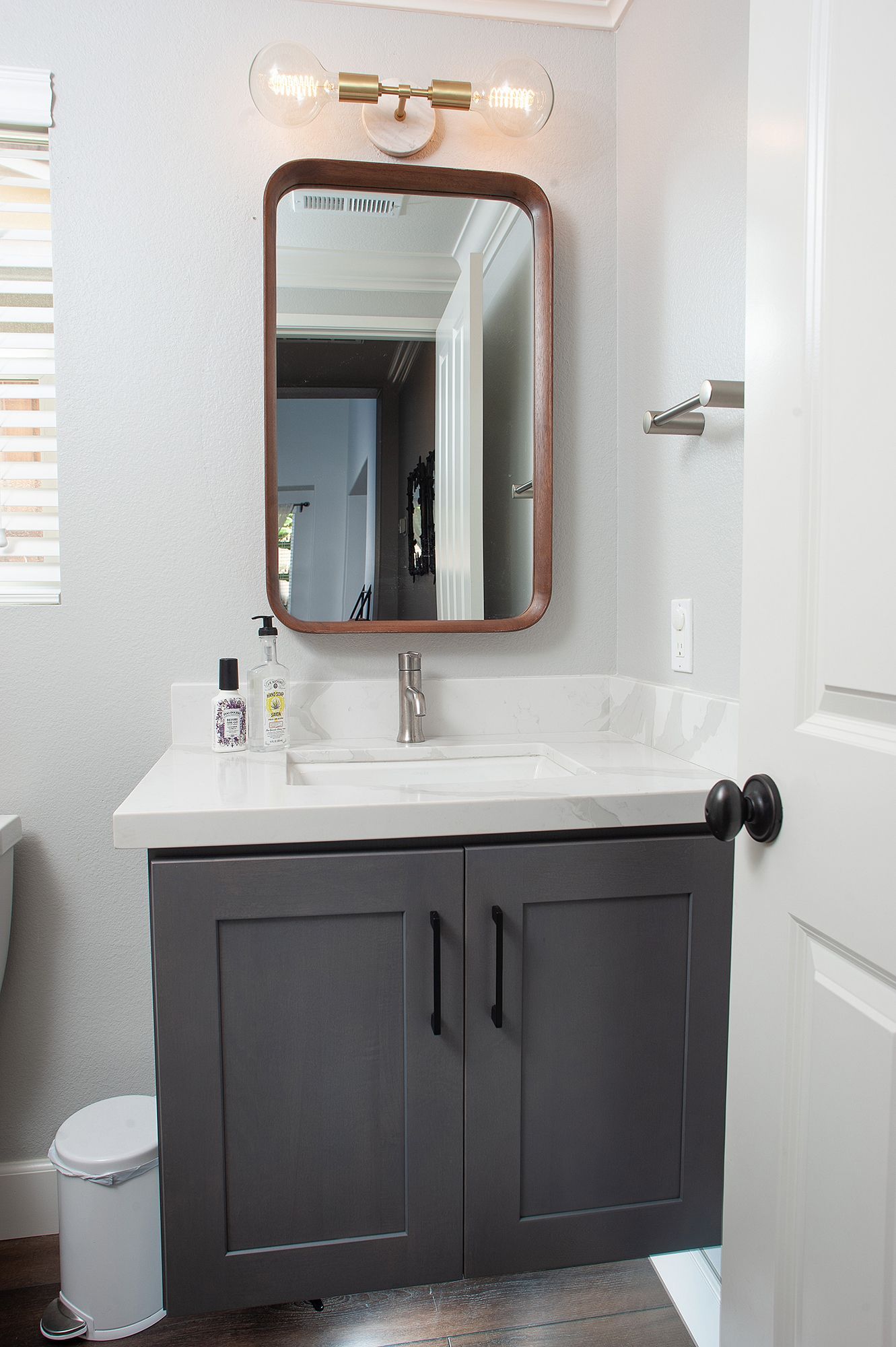 Small bathroom with gray vanity, rectangular mirror, white countertop, and light fixture.