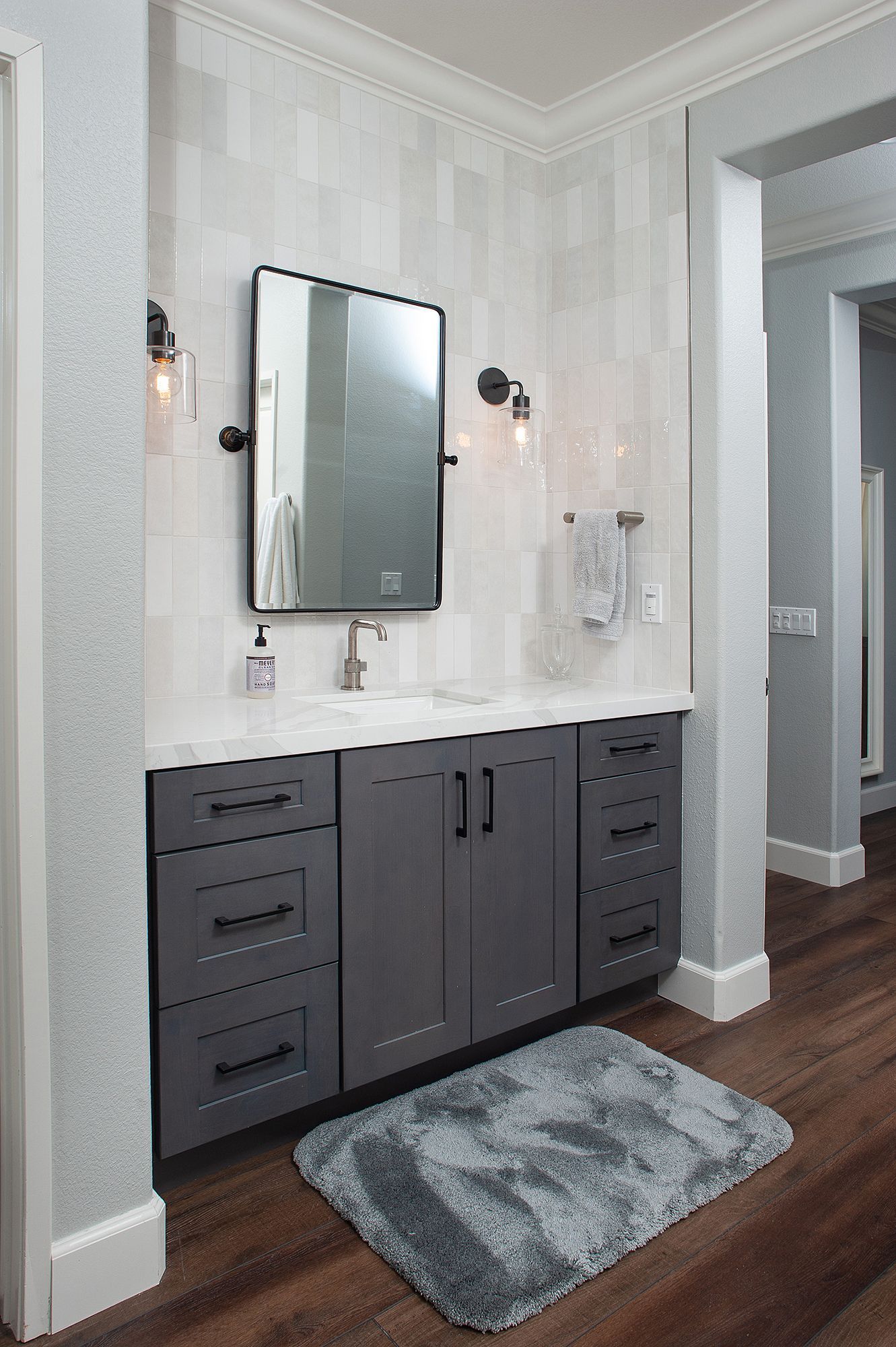Gray bathroom vanity with drawers, mirror, and wall sconces. Dark gray cabinets, white countertop.