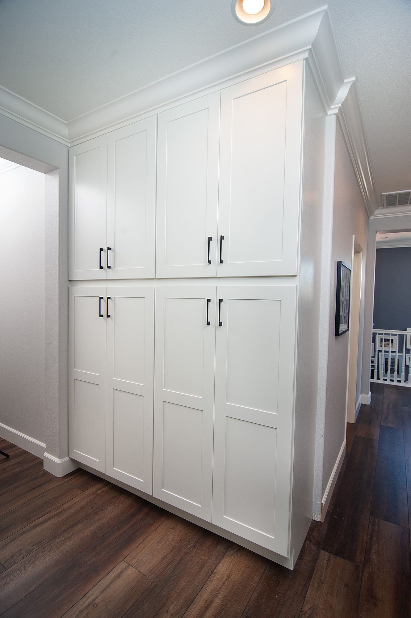White storage cabinets in a hallway with dark wood flooring and light walls.