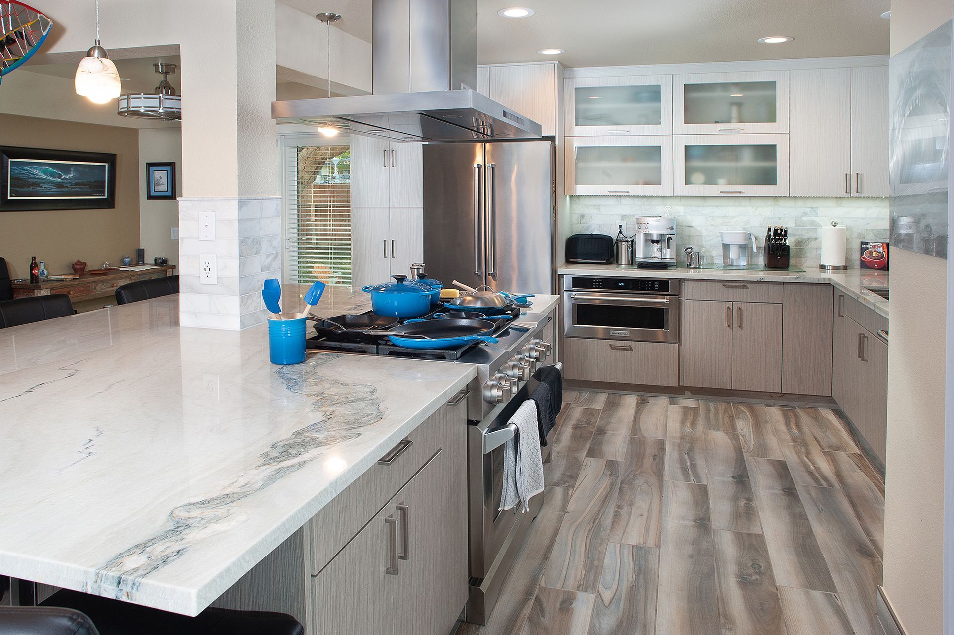 Modern kitchen with white countertops, stainless steel appliances, and wood-look flooring.