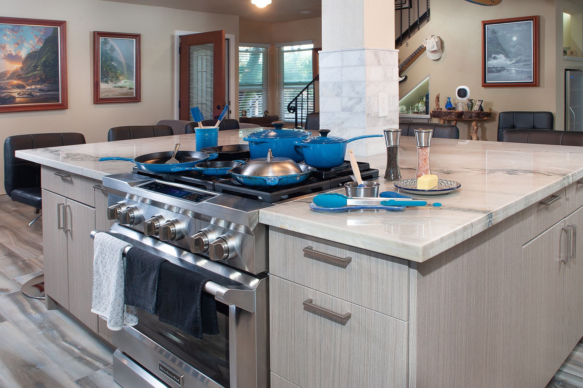 A modern kitchen with a large island, stainless steel stove, and blue cookware.