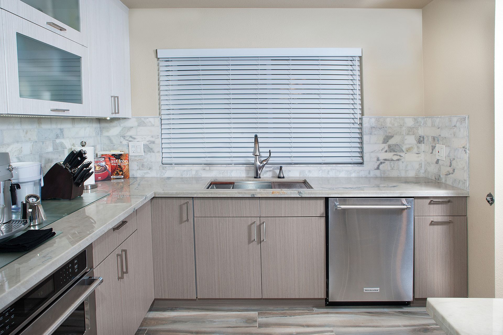 Modern kitchen with stainless steel appliances, light wood cabinets, and a window with blinds.