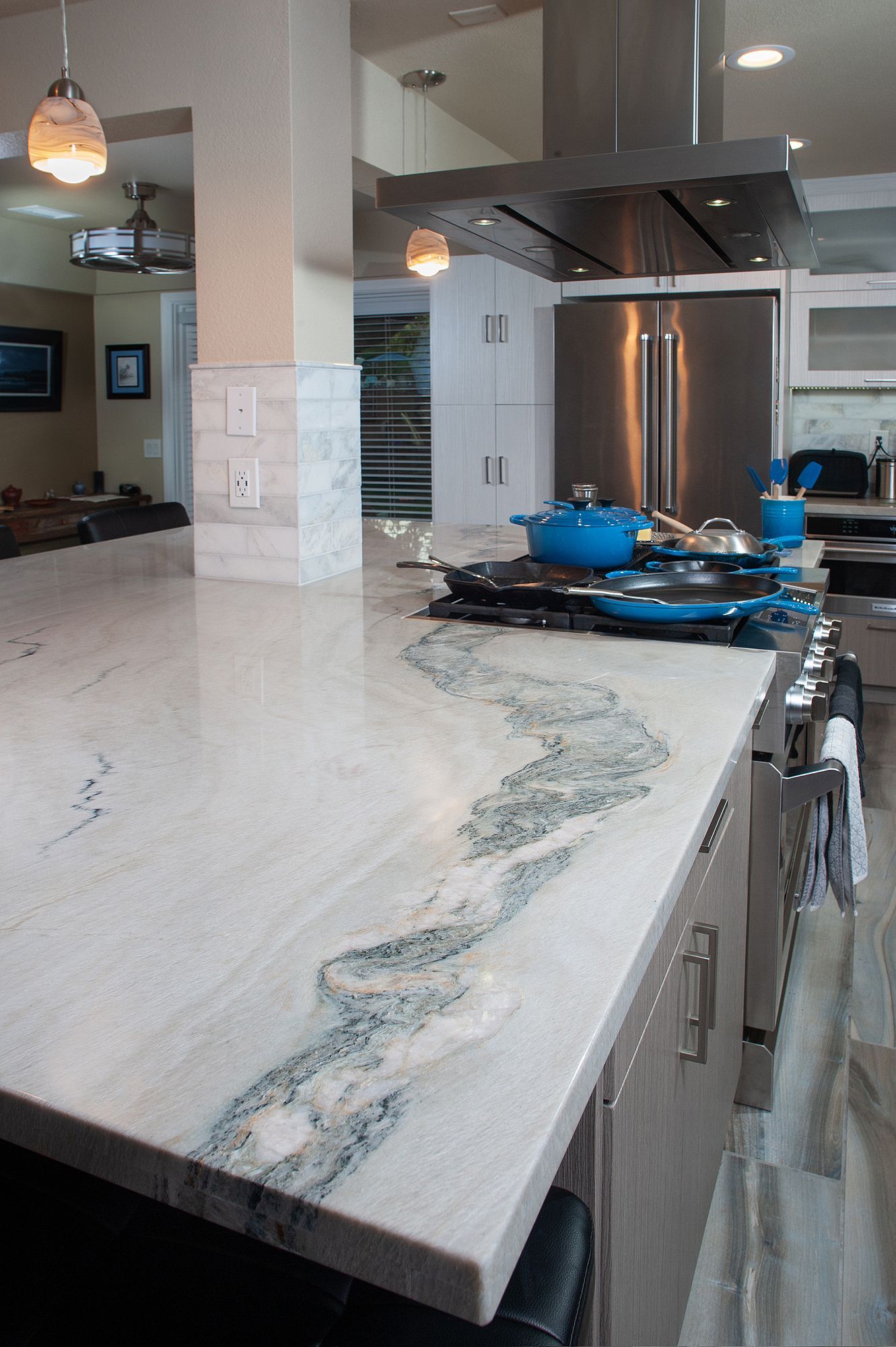 Granite countertop with blue-veined design in modern kitchen with stainless steel appliances and blue cookware.