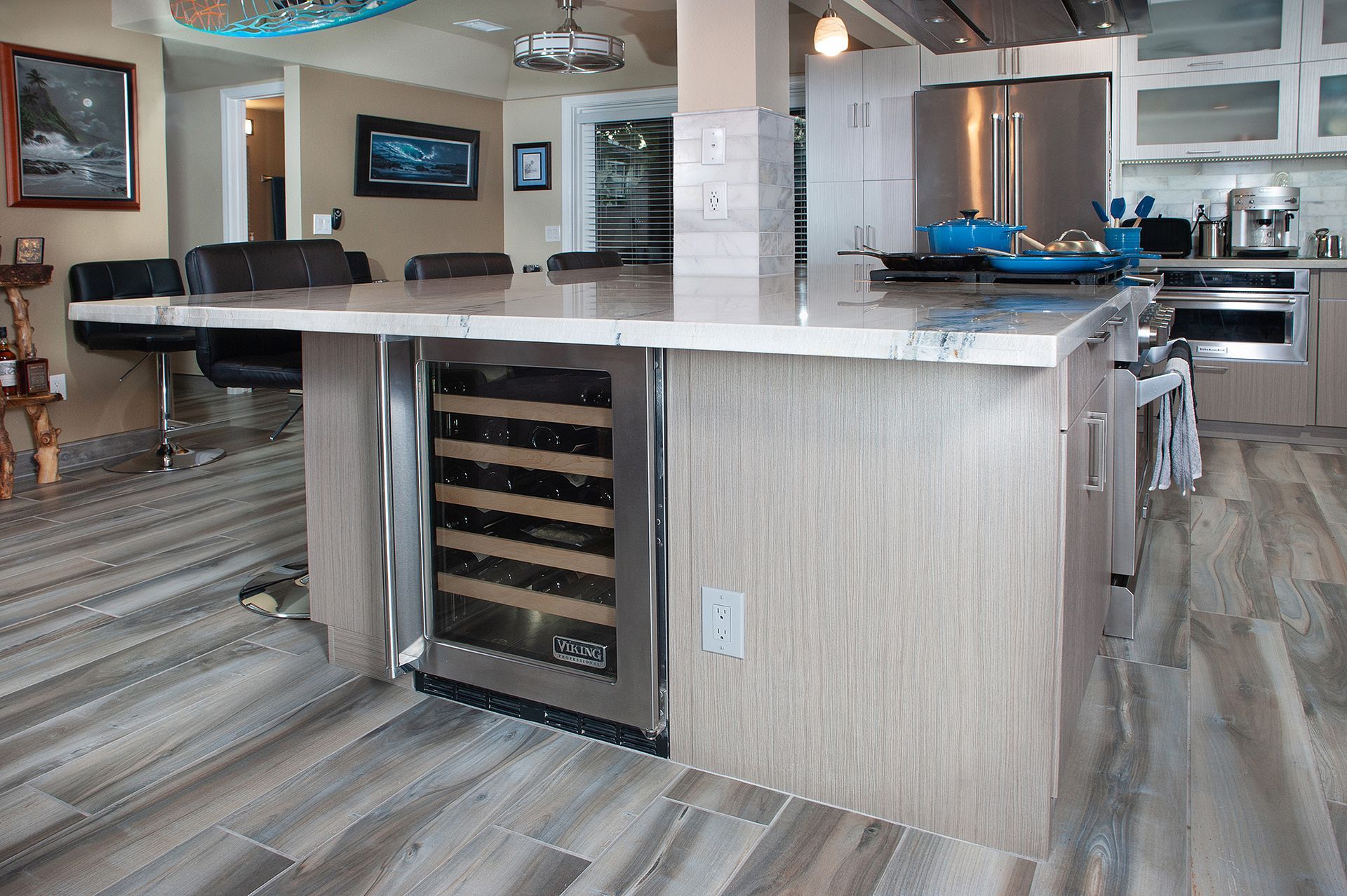 Kitchen island with built-in wine fridge, light wood cabinets, stone countertop.