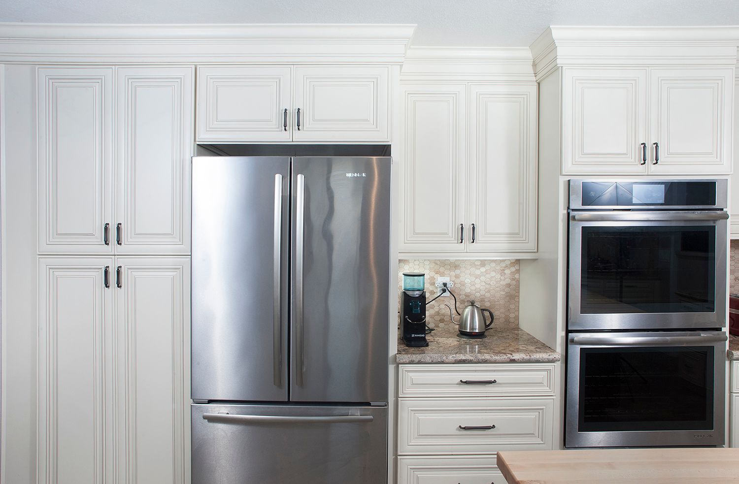 White kitchen cabinets frame a stainless steel refrigerator and double ovens.