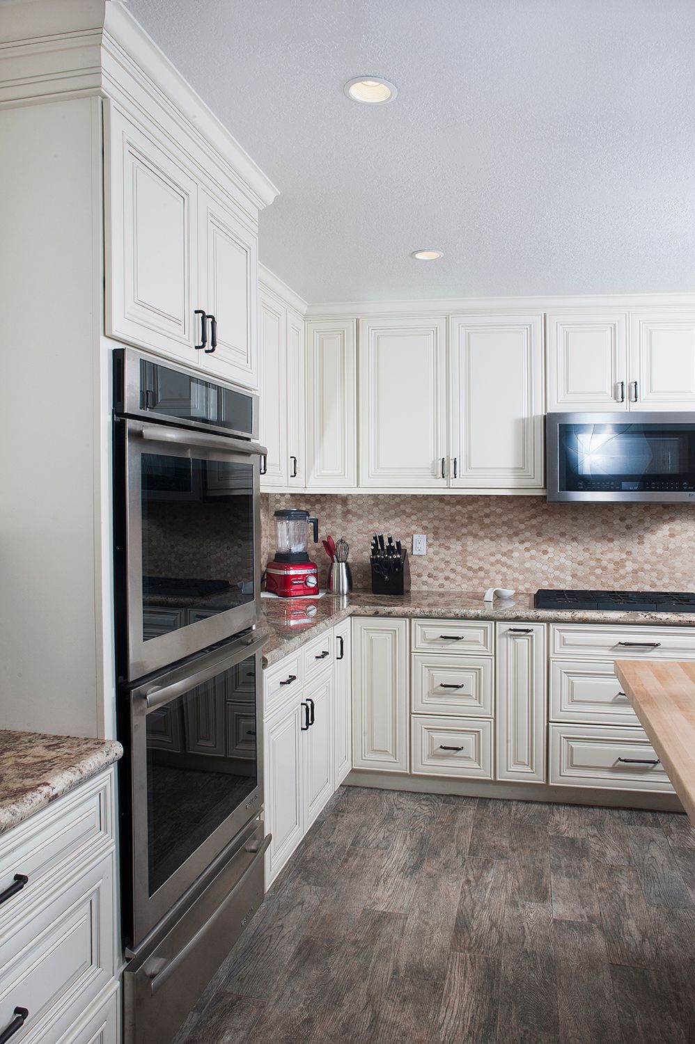 White kitchen with built-in double oven and microwave. Light cabinets, stone countertops, and brown floors.