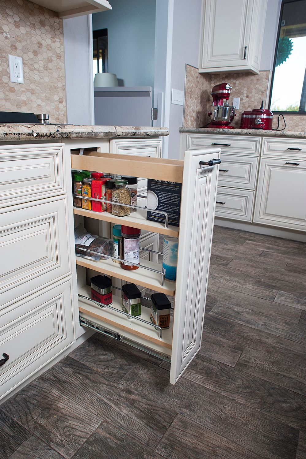Pull-out spice rack in a white kitchen cabinet, filled with spices and condiments.