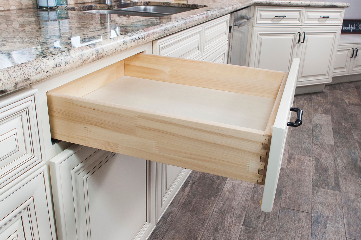 Open kitchen drawer, light wood construction, with a white cabinet in the background.
