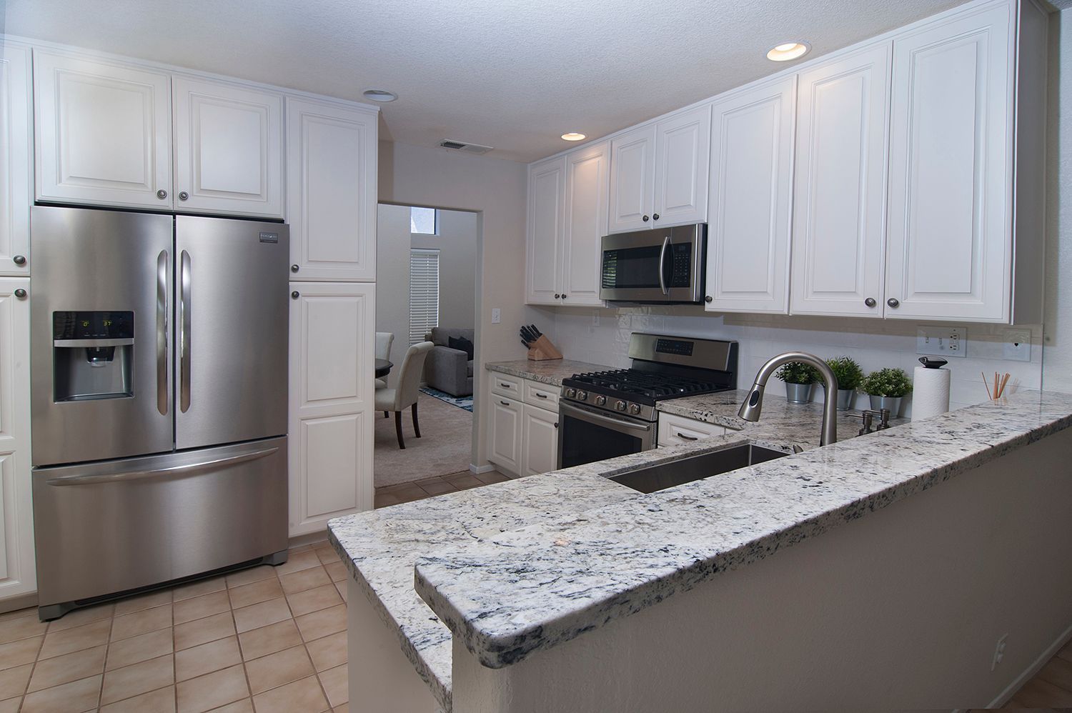 White kitchen with stainless steel appliances and granite countertop.