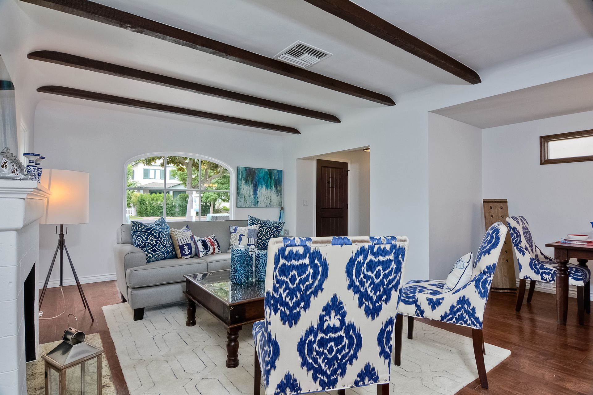 Living room with white walls, dark wood beams, blue patterned chairs, and grey sofa.