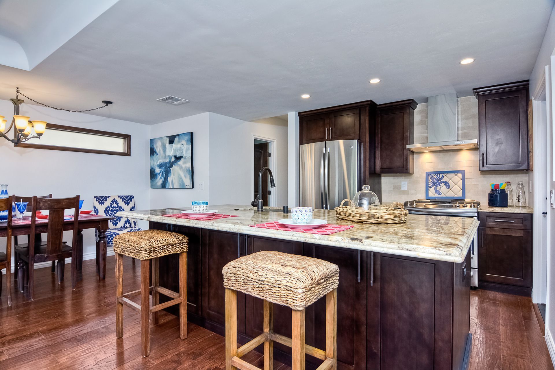 Open-concept kitchen with dark cabinets, island with stools, dining area with table, and stainless steel appliances.