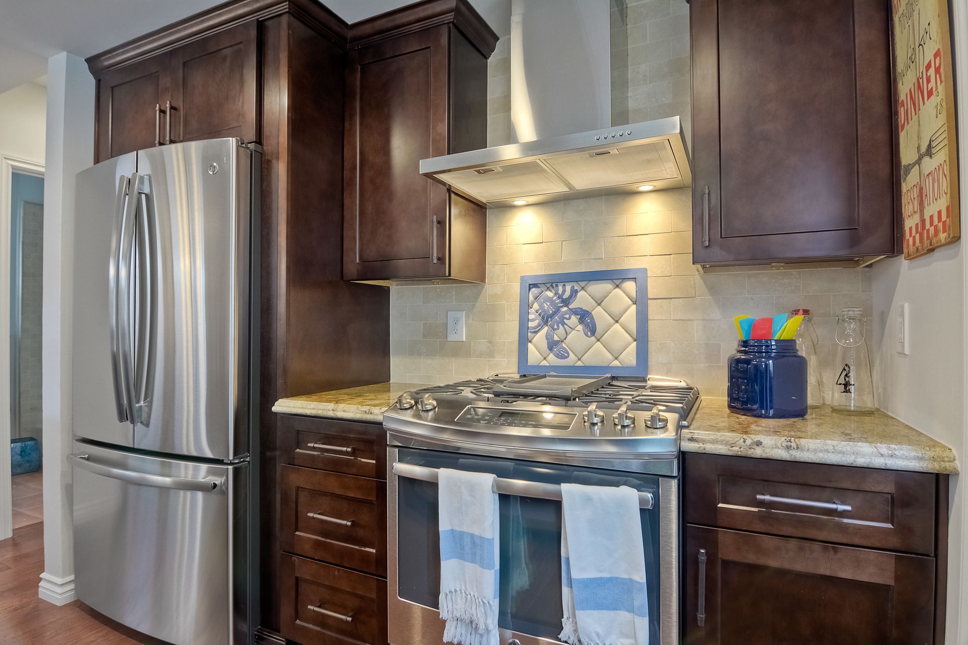 Stainless steel fridge next to dark brown cabinets and a gas range in a kitchen.