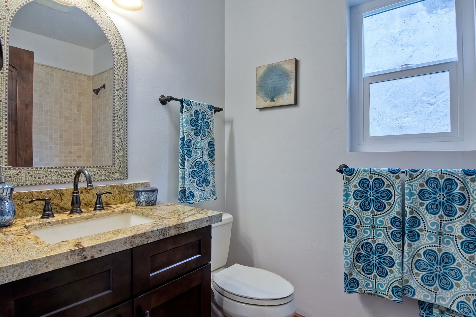 Bathroom with dark wood vanity, patterned blue towels, and small window.