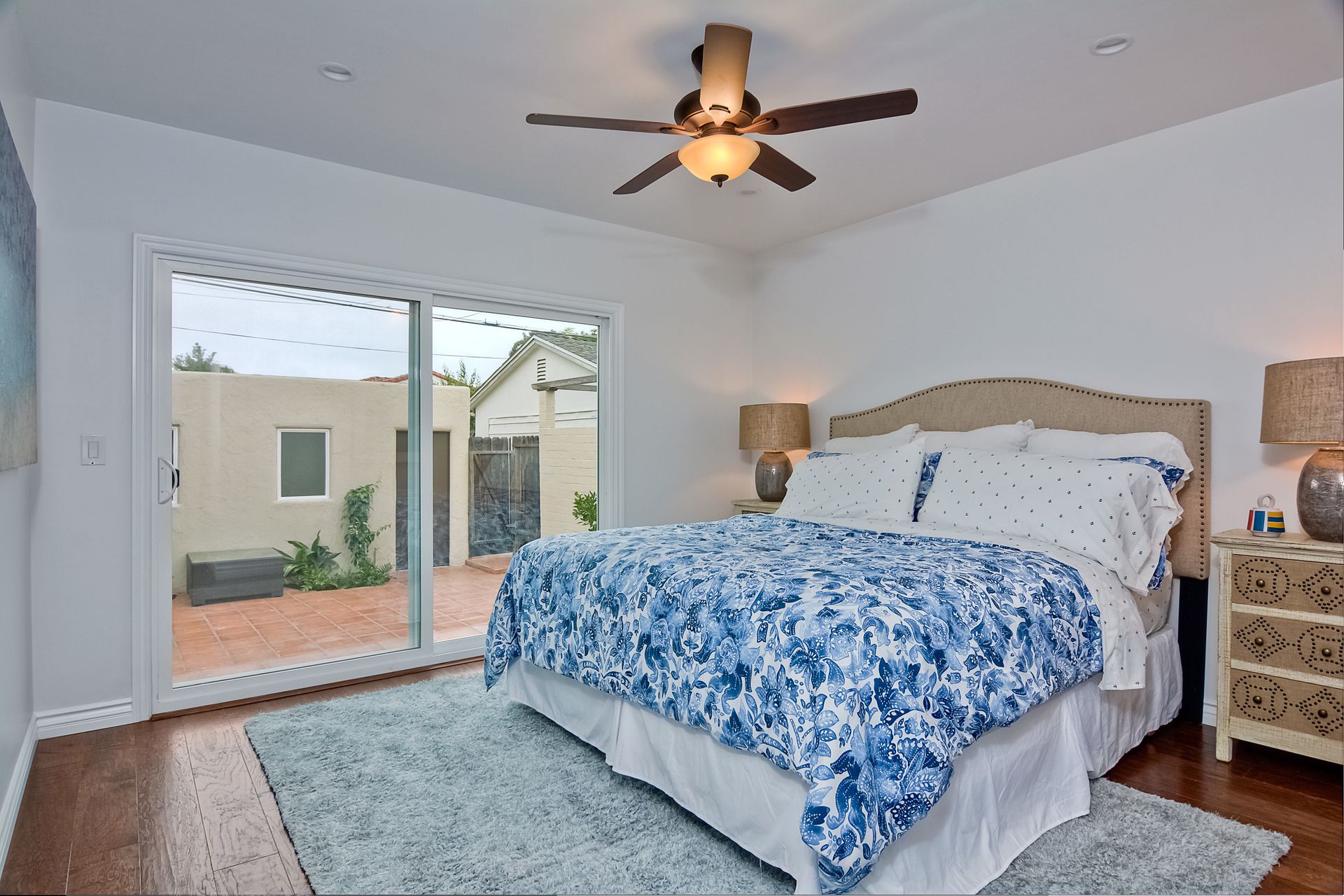Bedroom with a blue and white floral bedspread, sliding glass door, and a view of a patio.