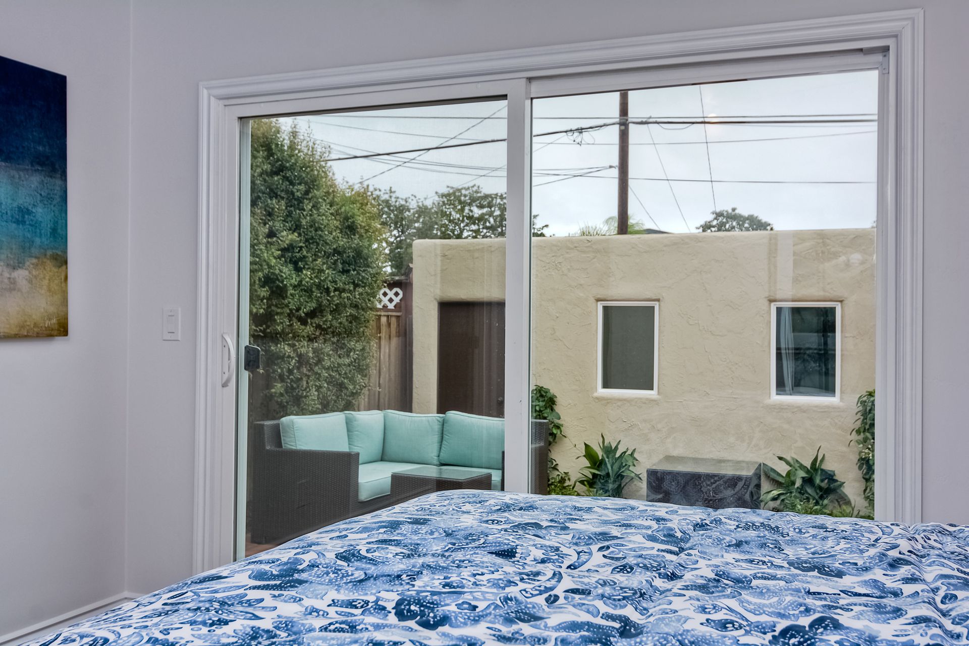 Bedroom with sliding glass door overlooking outdoor seating and a stucco building.