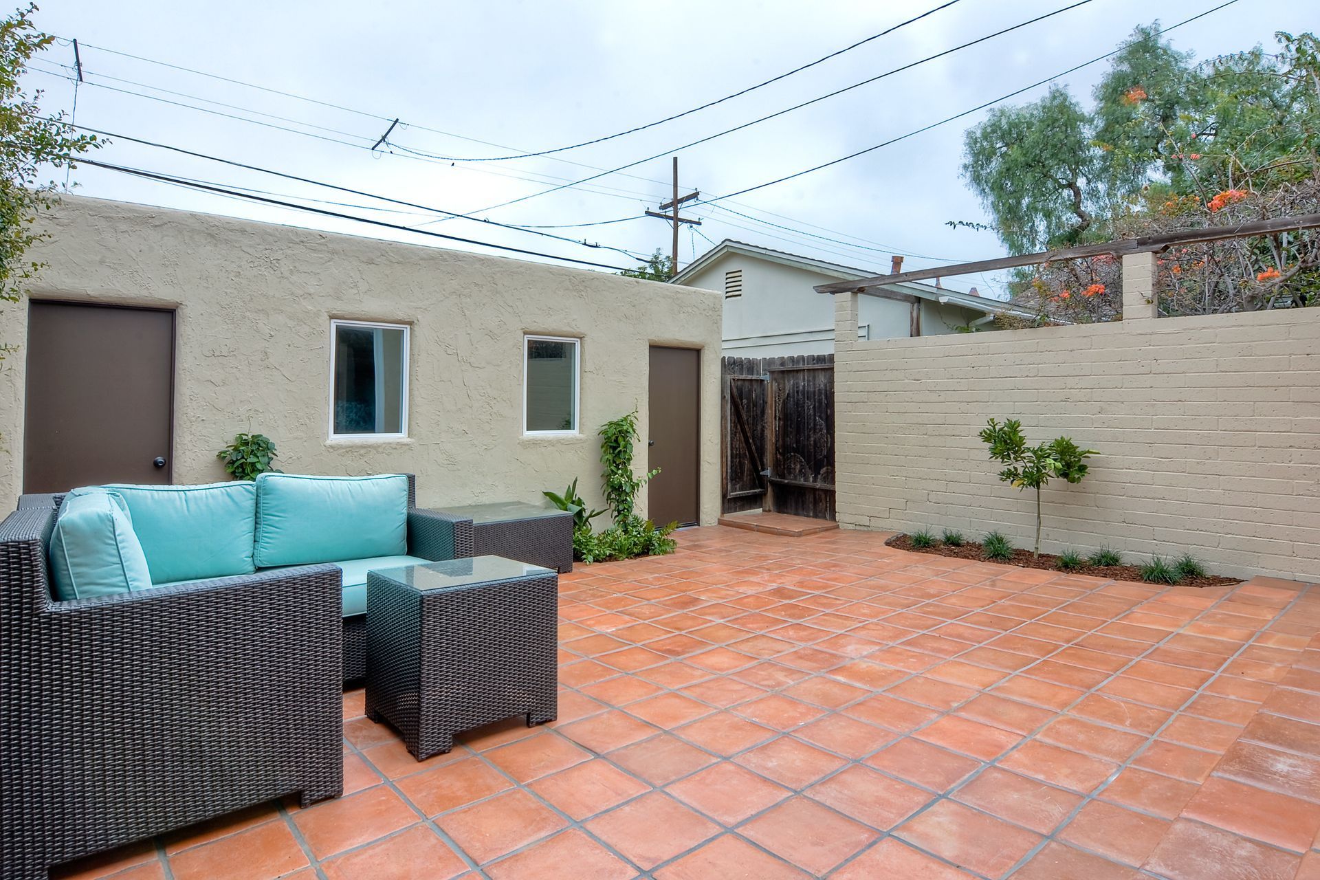 Patio with turquoise seating, brown doors, terracotta tiles, and a beige wall under cloudy skies.