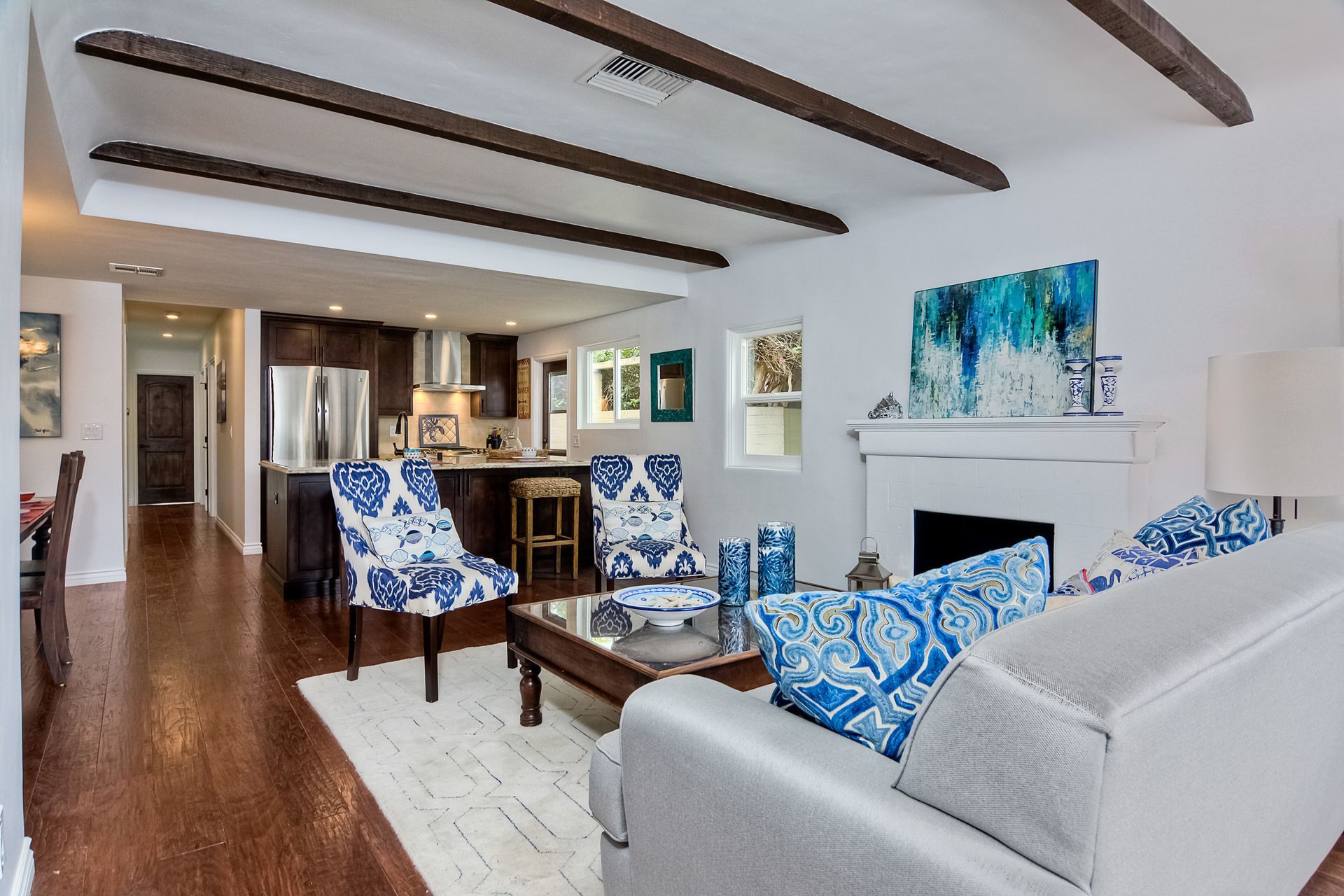 Living room with exposed beams, open to kitchen, and blue and white accents.
