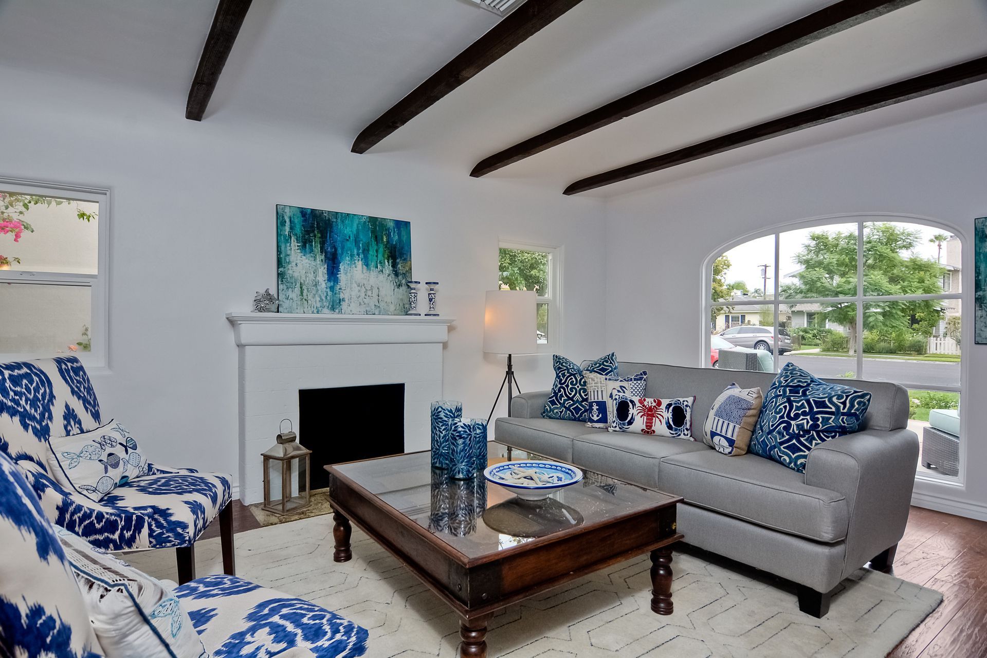 Living room with white walls, gray sofa, blue accents, and wooden beams.