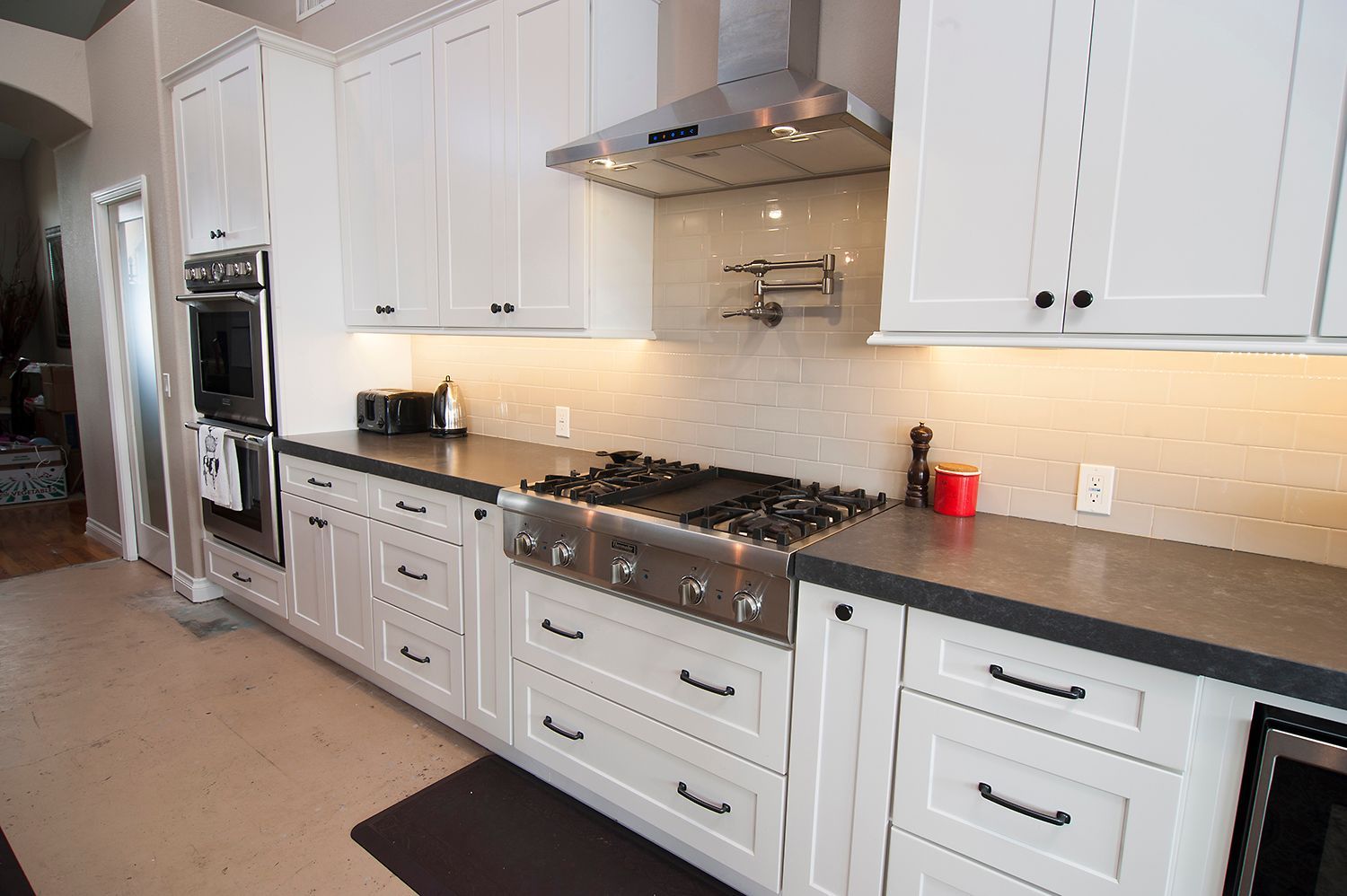 White kitchen with stainless steel appliances, black countertops, and white cabinets.