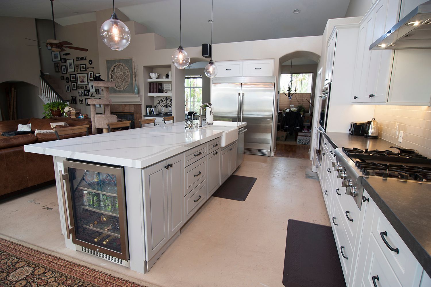 Spacious white kitchen with island, beverage cooler, stove, and archway to another room.