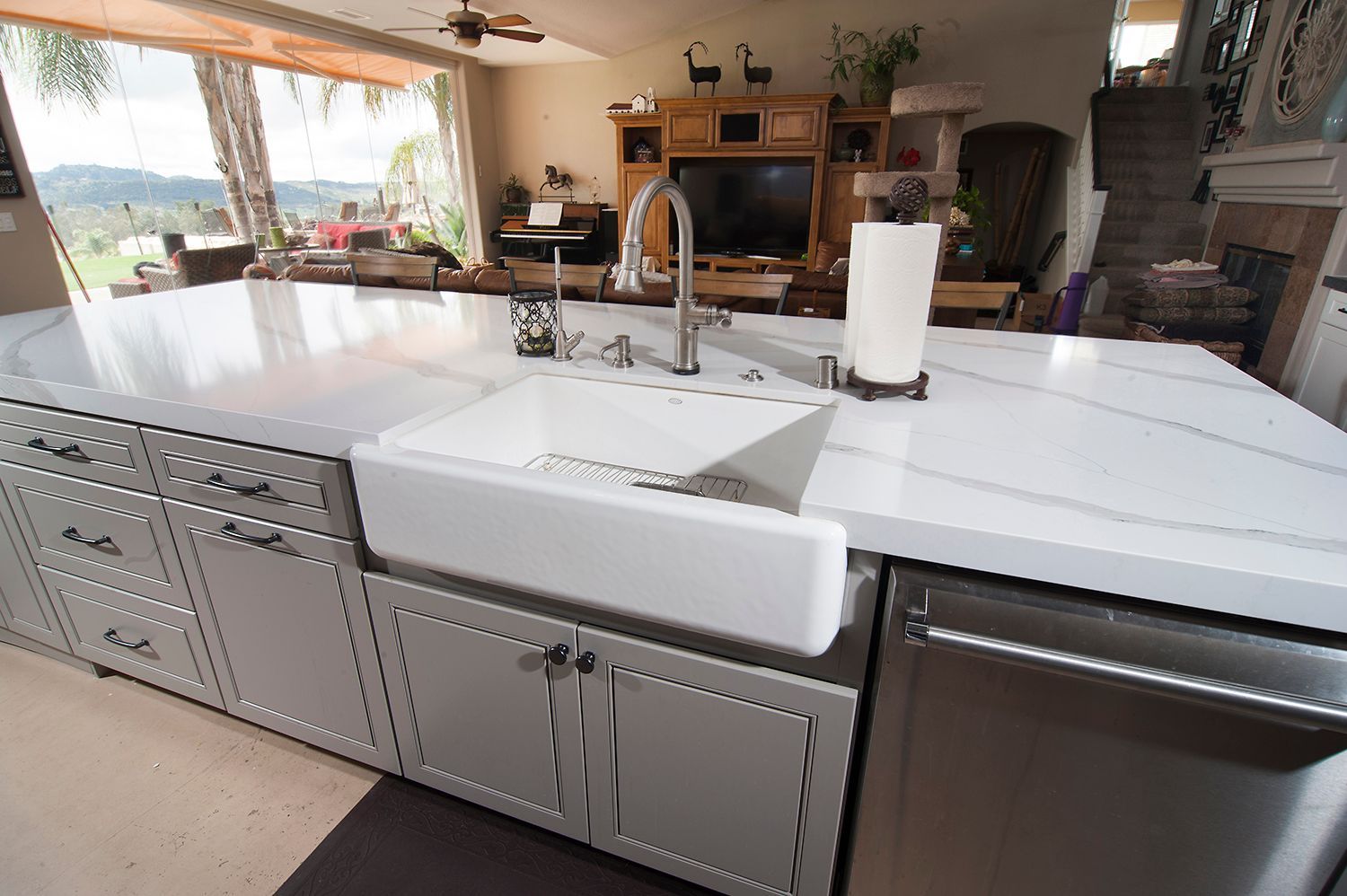 Kitchen island with white countertops, farmhouse sink, and stainless steel dishwasher.