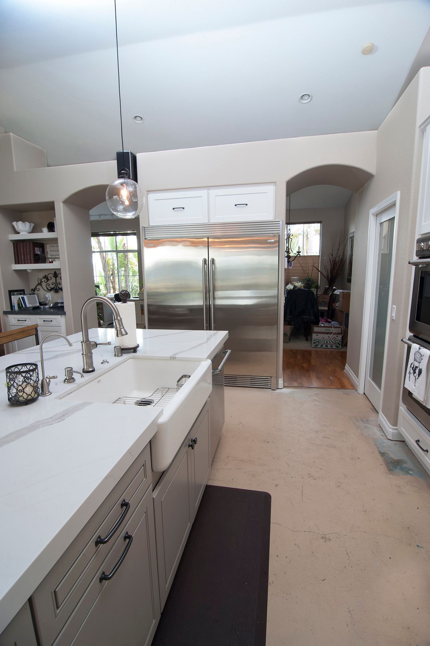 Modern kitchen with stainless steel refrigerator, white countertops, and arched doorways.