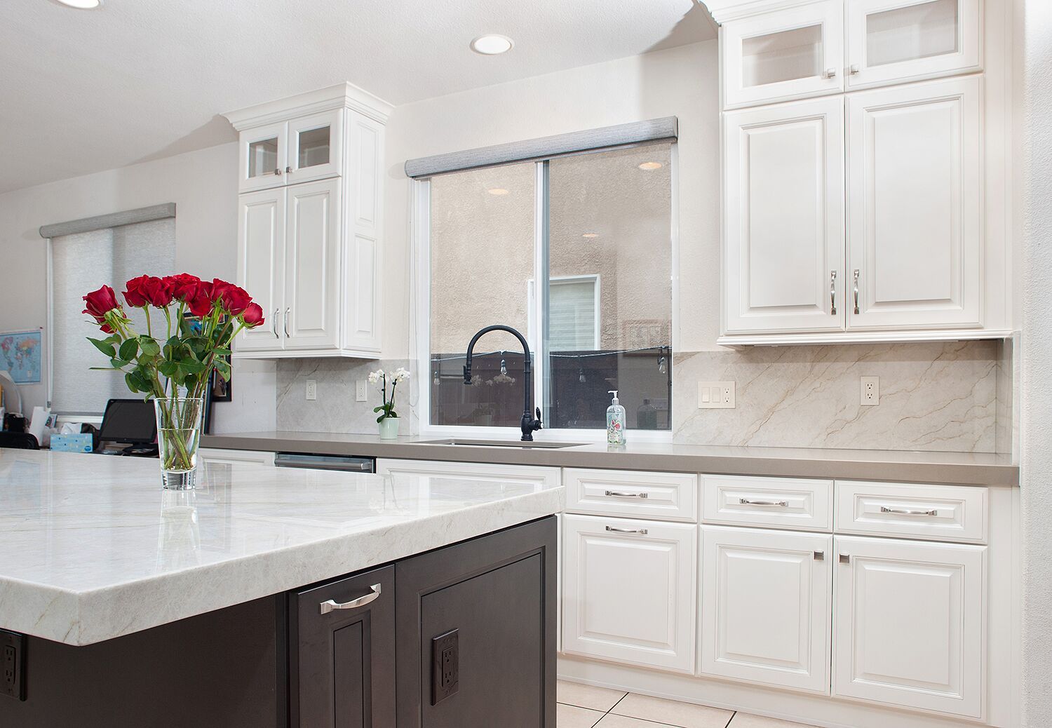 White kitchen with island, cabinets, and a window over the sink; red roses in a vase.