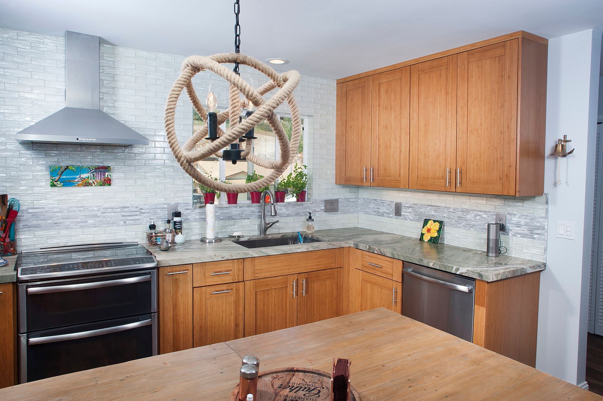 Kitchen with light wood cabinets, rope chandelier, and stainless steel appliances.