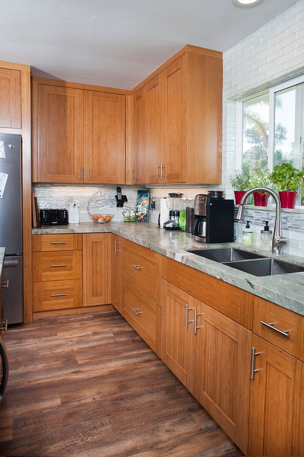 Wooden kitchen with cabinets, sink, countertop, and window with plants.