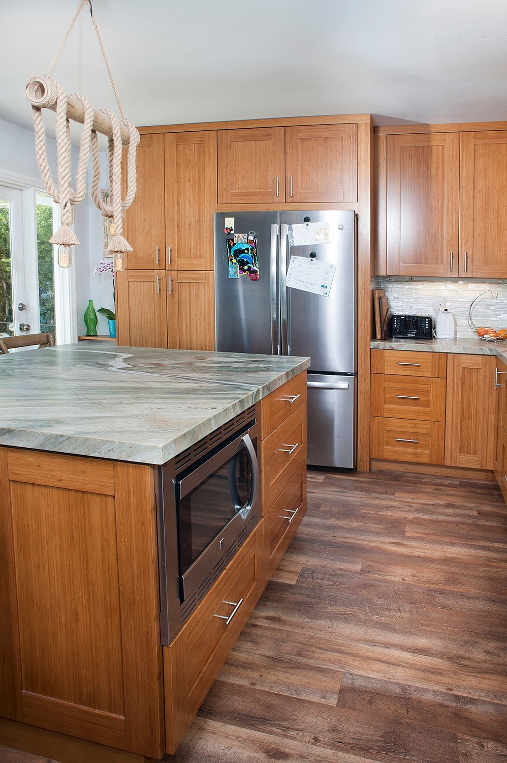 Kitchen with wood cabinets, granite countertop island, stainless steel refrigerator, microwave, and wood-look flooring.
