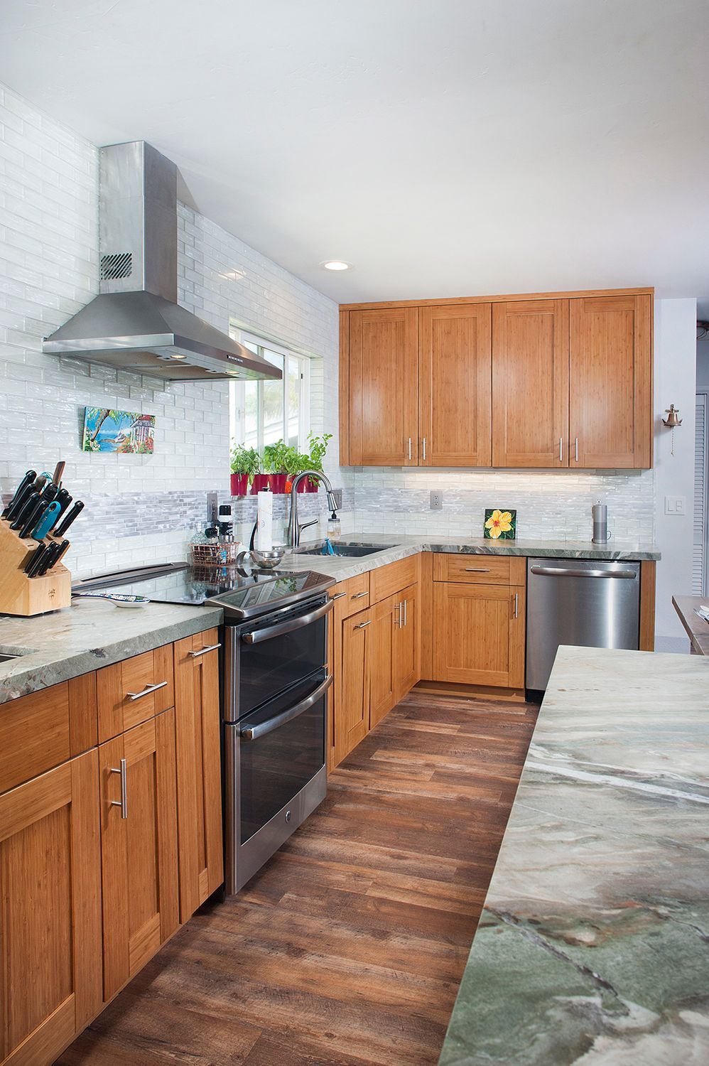 Wooden kitchen with light countertops, stainless steel appliances, and a white brick backsplash.