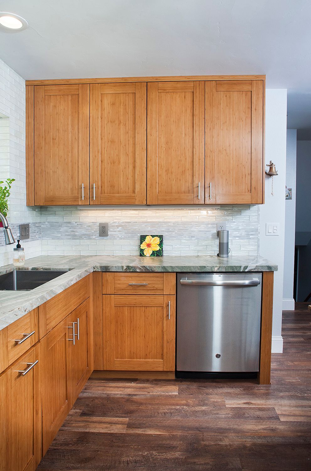Kitchen with light-brown cabinets, stainless steel dishwasher, and speckled countertops. Wooden floors.