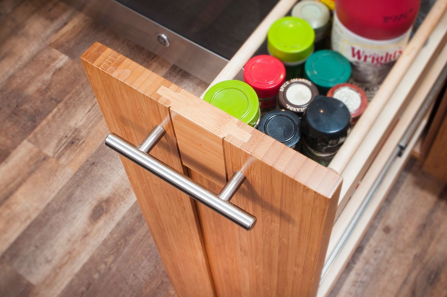 Wooden spice rack drawer filled with colorful spice jars, opened, in a kitchen.
