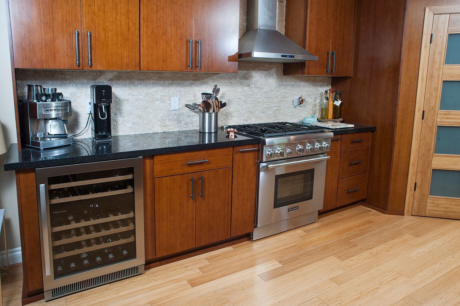 Modern kitchen with wood cabinets, stainless steel appliances, black countertops, and light wood floors.