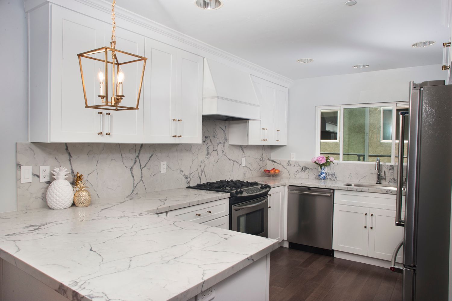 White kitchen with marble countertops, stainless steel appliances, and gold light fixture.