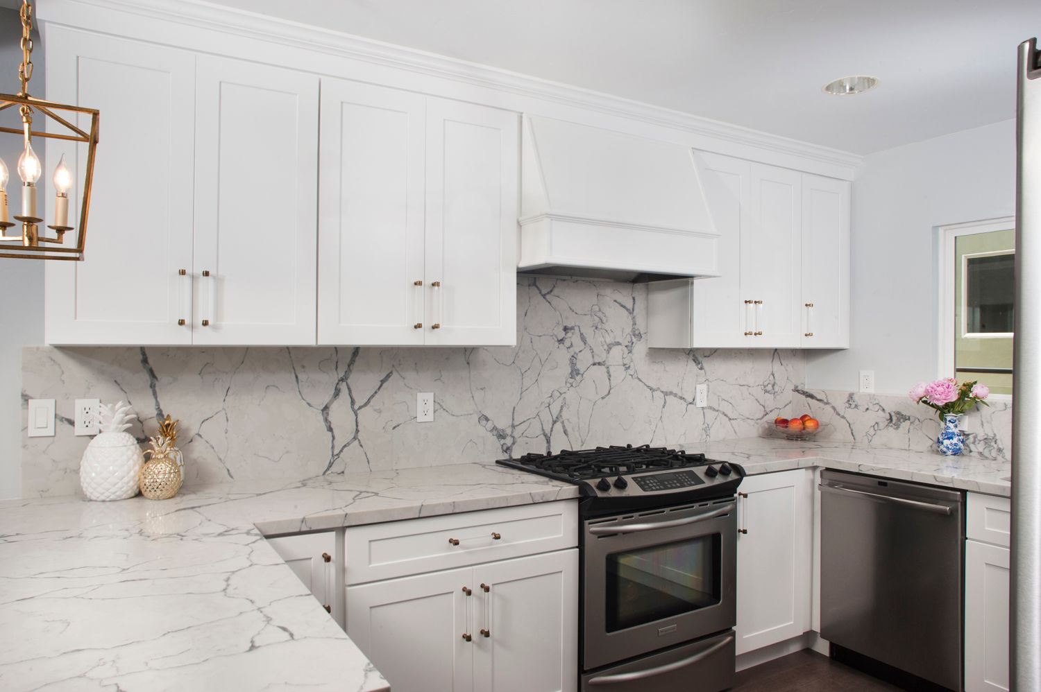 White kitchen with marble countertops and stainless steel appliances.