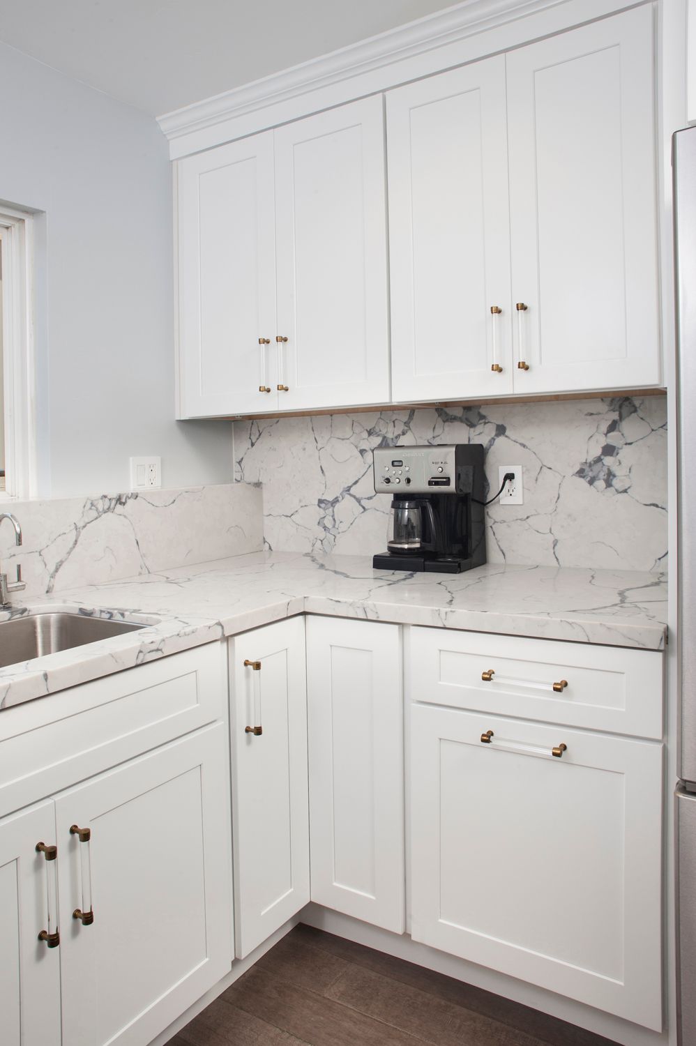 White kitchen cabinets with marble backsplash and built-in espresso machine.