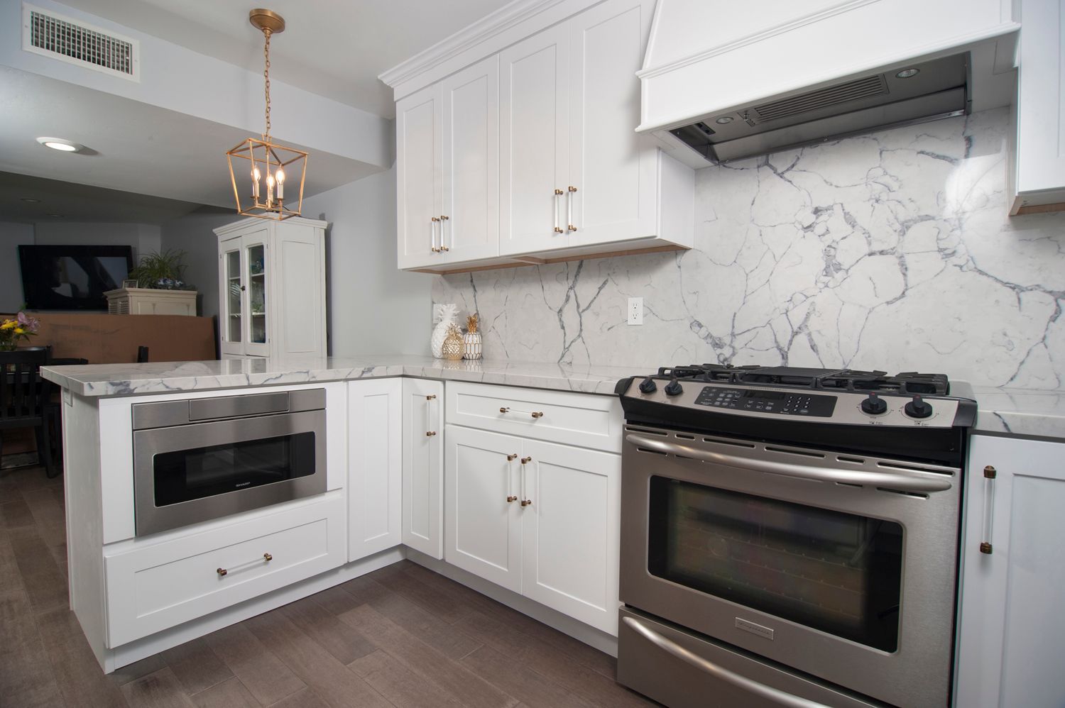 White kitchen with stainless steel appliances, marble backsplash, and light wood floors.