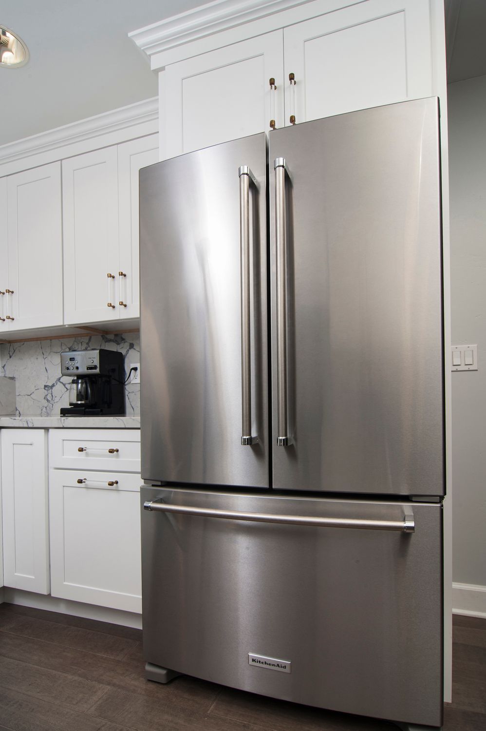 Stainless steel refrigerator in a white kitchen with cabinetry.