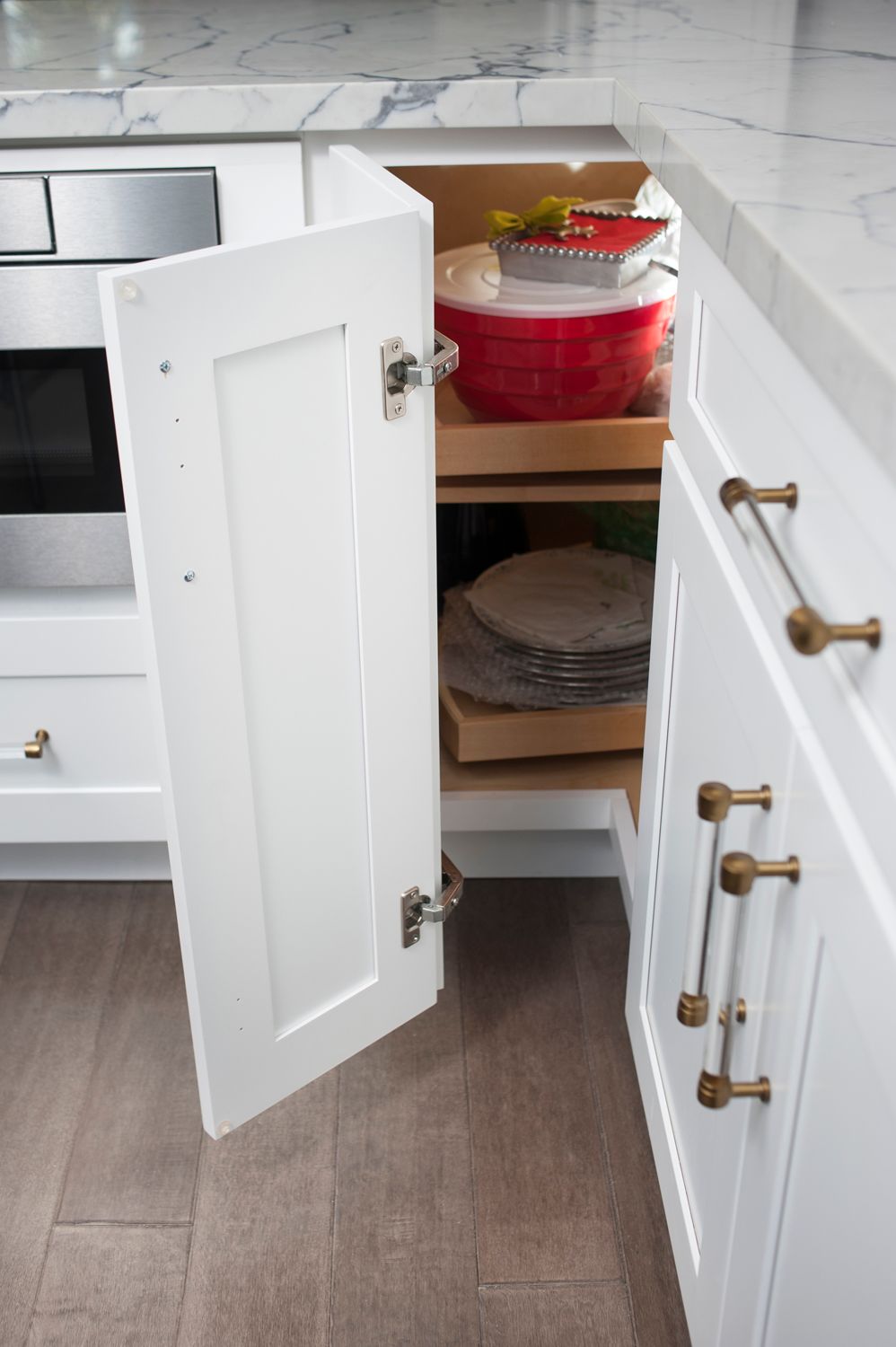 White kitchen cabinet open, revealing pull-out shelves with red bowl and plates.