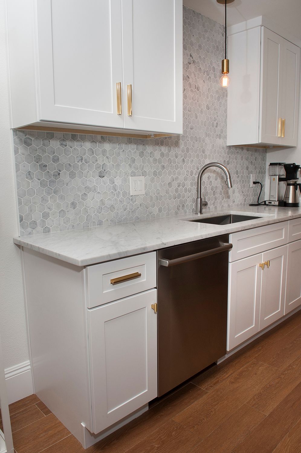 White kitchen with marble countertops, stainless steel appliances, and hexagon tile backsplash.