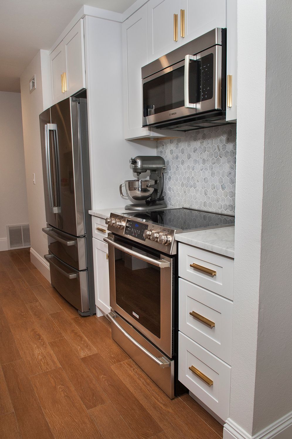 Small modern kitchen with stainless steel appliances, white cabinets, and wood floors.