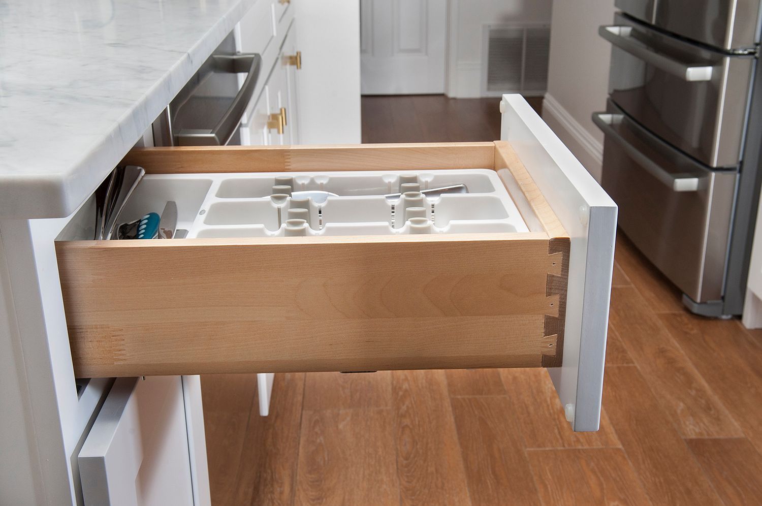 Open kitchen drawer with silverware organizer. Drawer is wood with white face, on a white cabinet.