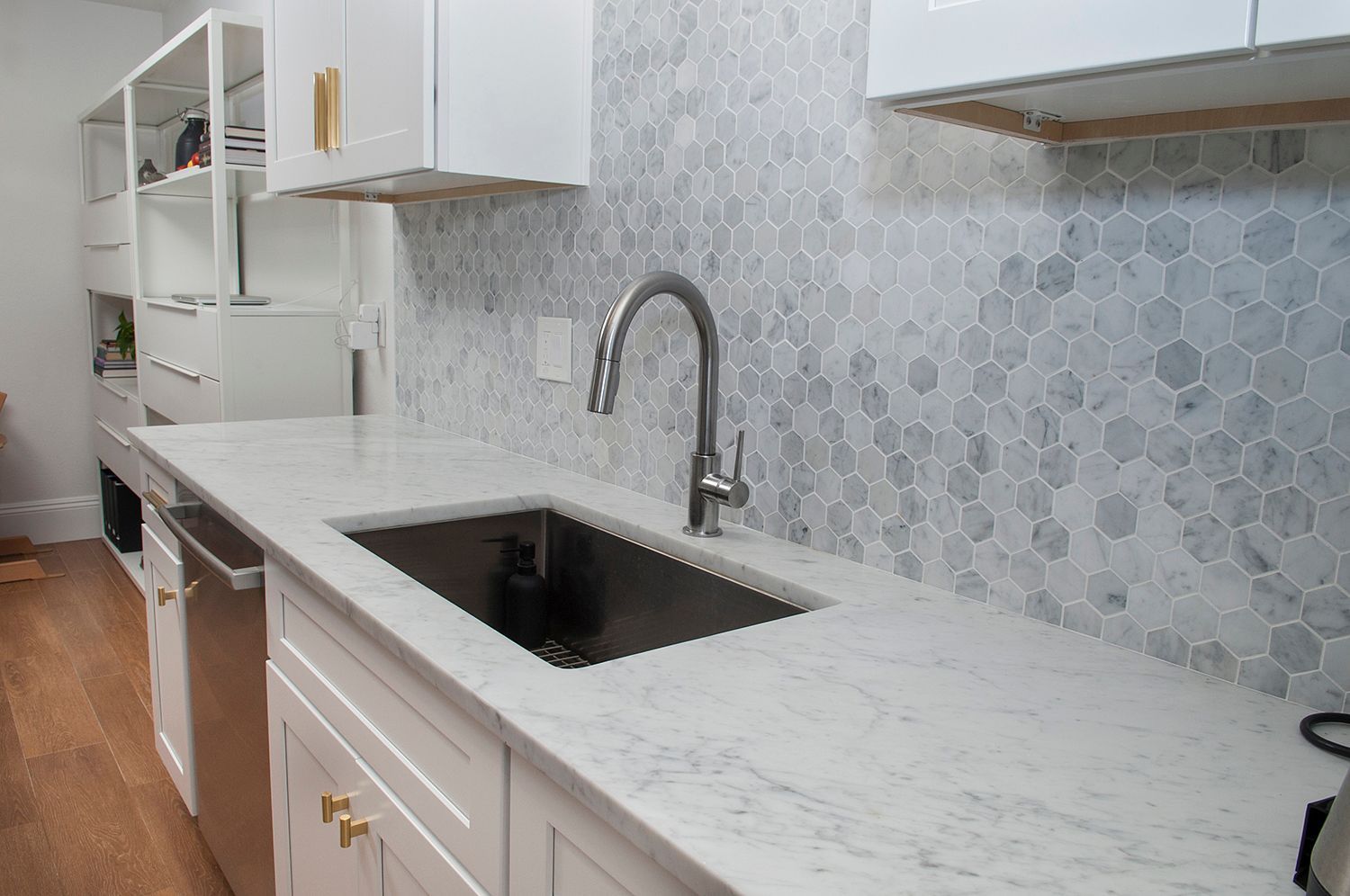Modern kitchen with white cabinets, marble countertop, hexagonal backsplash, stainless steel sink, and faucet.