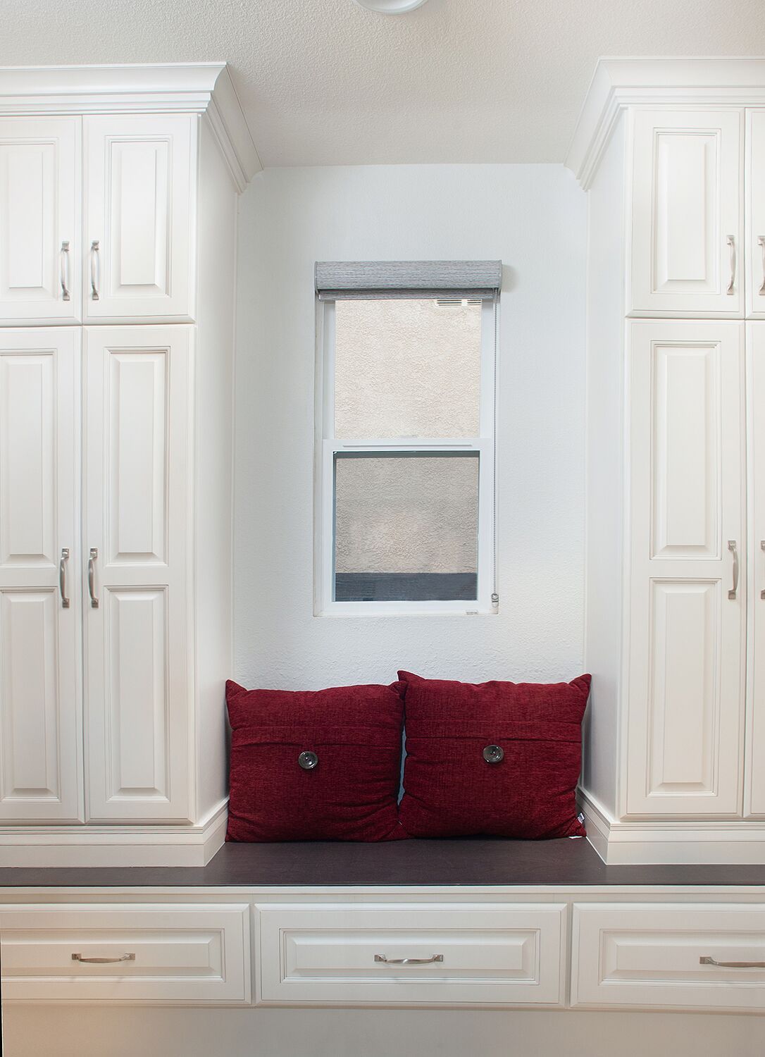 Built-in white cabinets flanking a window with red pillows on a bench.